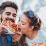 Couple eating pizza outdoors and smiling.They are sharing pizza in an outdoor cafe.