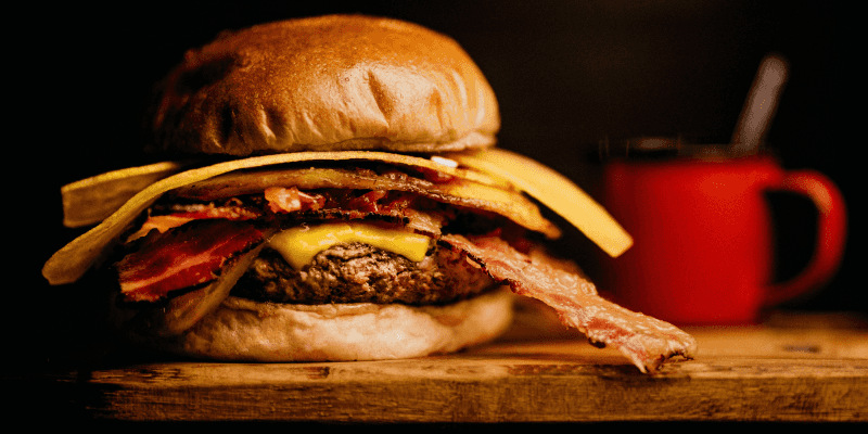 Bacon and Ham Burger on Wooden Table with Red Cup in the Background 