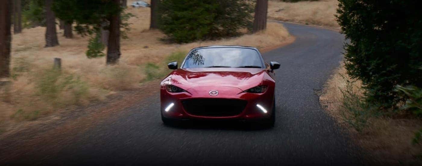 A red 2023 Mazda MX-5 is shown driving on a winding road.