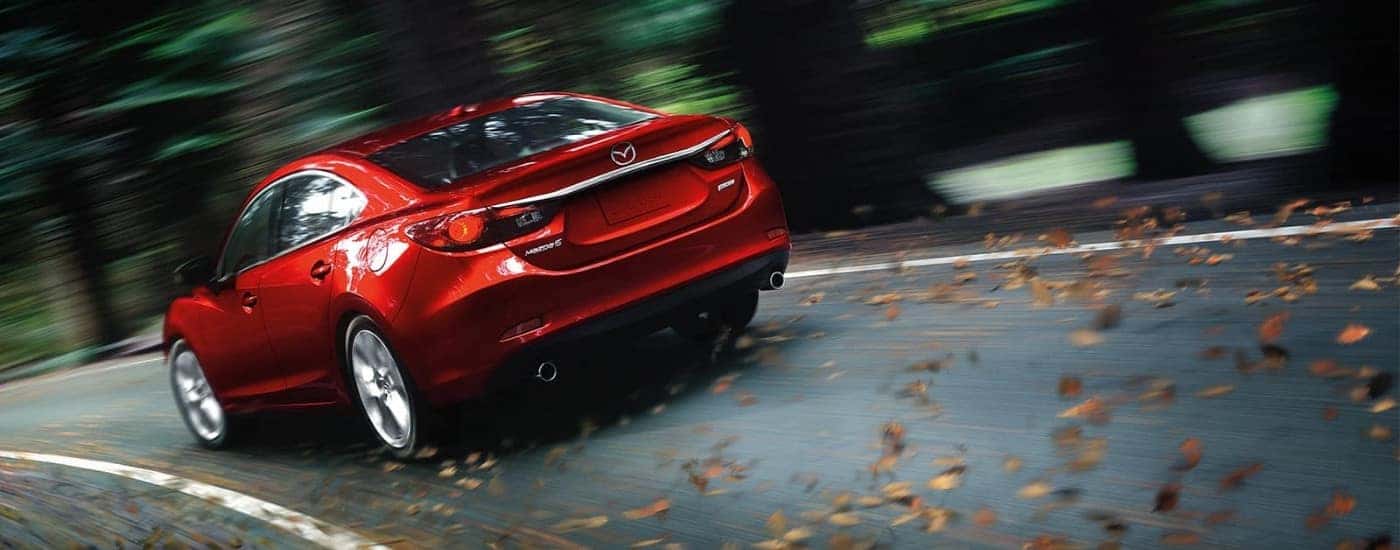 A red 2015 Mazda6 is shown from the rear driving on a tree-lined road.
