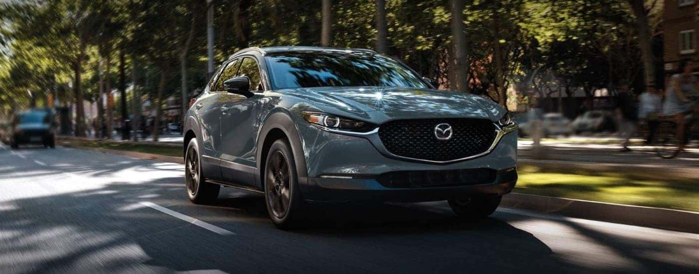 A grey 2023 Mazda CX-30 is driving on a tree-line road.