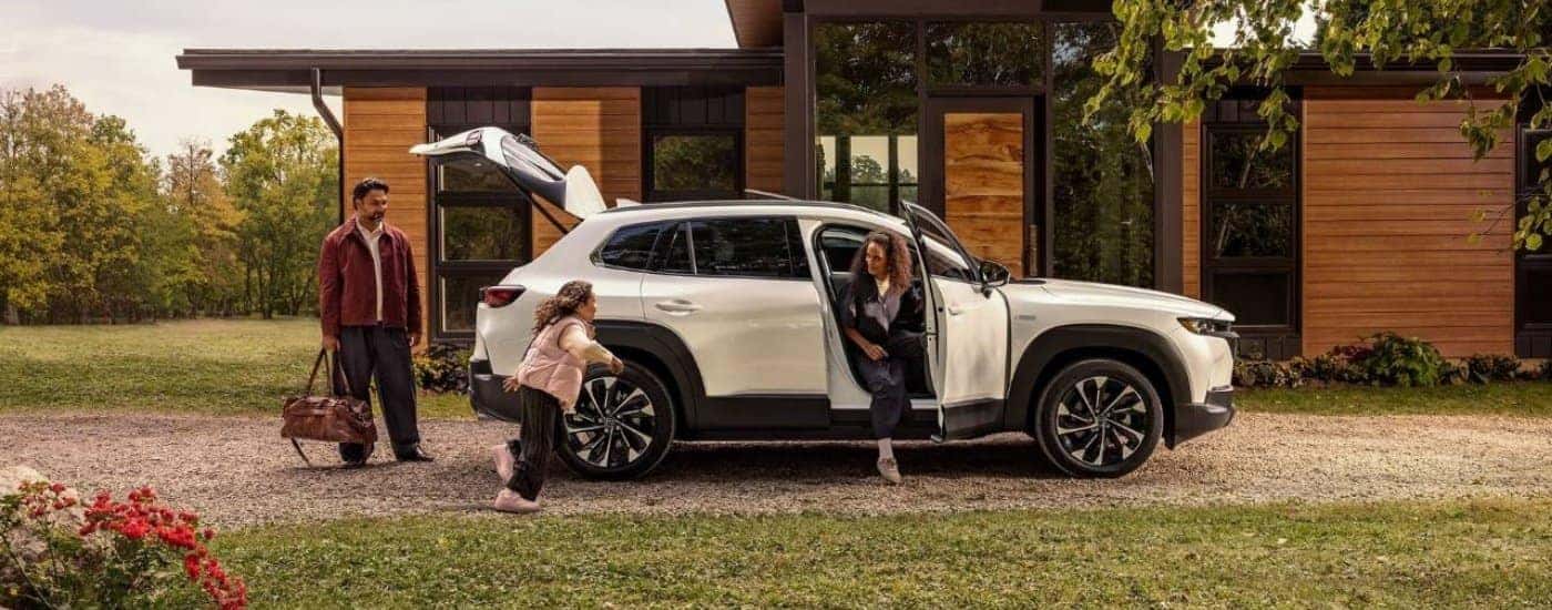 A white 2025 Mazda CX-50 Hybrid is parked in front of a house.