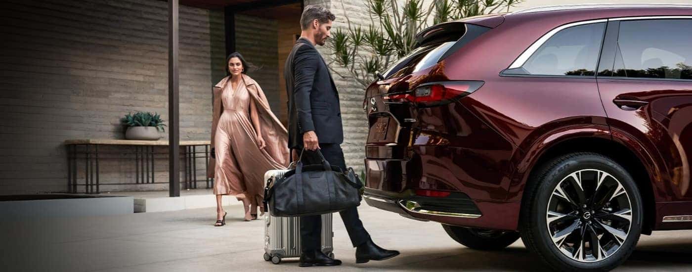 A person is stowing luggage in a red 2024 Mazda CX-90.