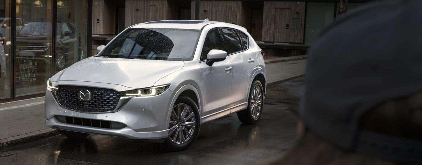 A white 2025 Mazda CX-5 parked in front of a shop.