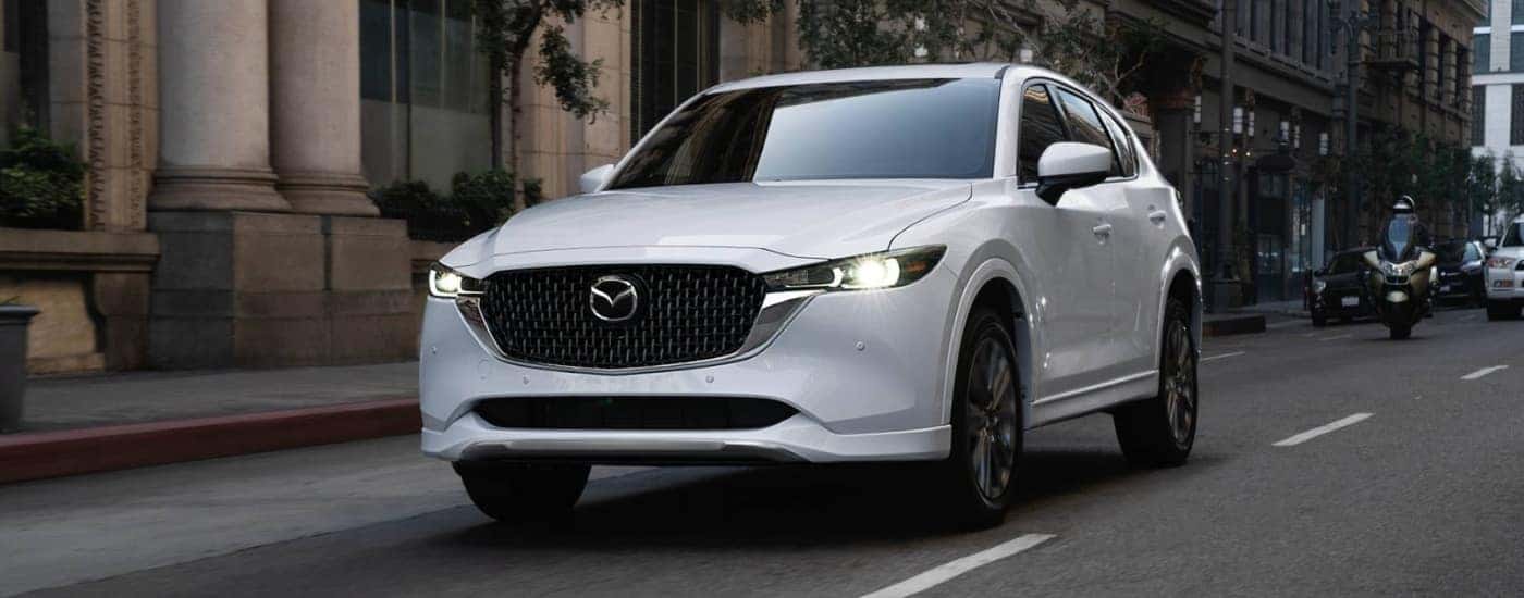 A white 2025 Mazda CX-5 for sale near Hartford driving on a city street.