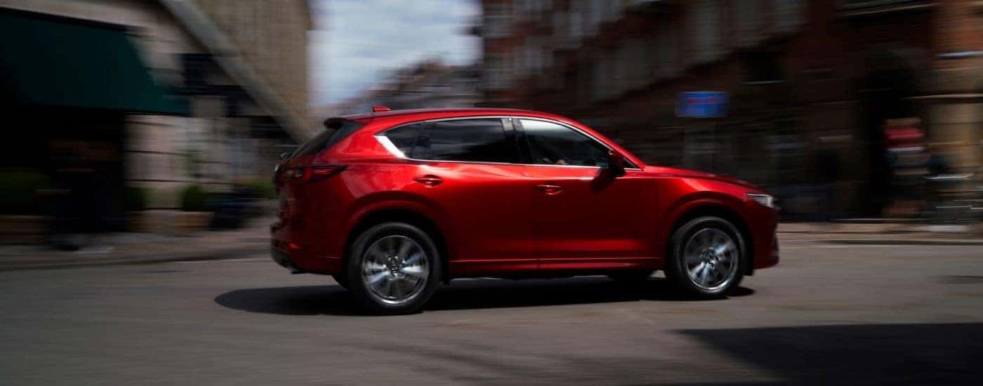 A red 2025 Mazda CX-5 for sale near Windsor driving on a city street.