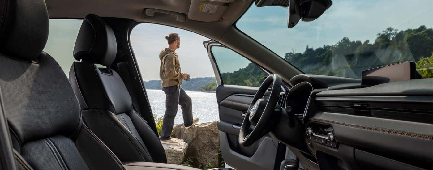 Man standing outside of a 2025 Mazda CX-50 hybrid near a lake