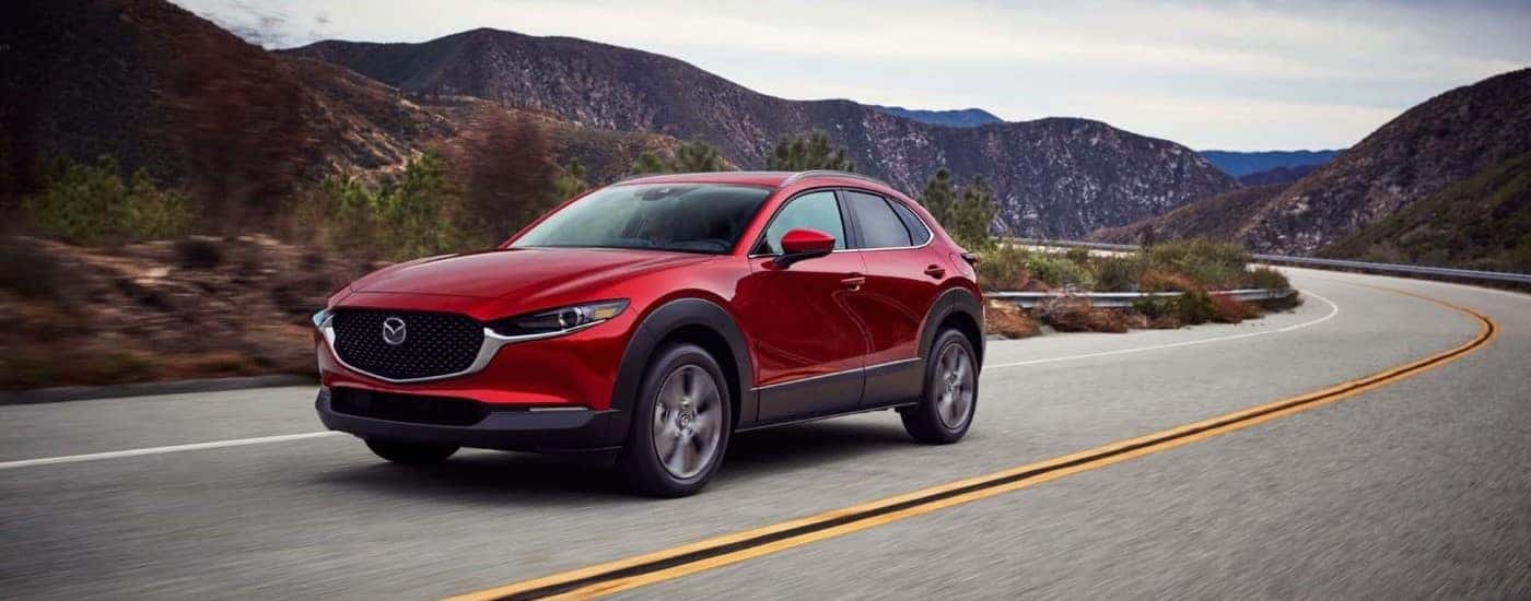 A red 2025 Mazda CX-30 is shown driving to visit a Mazda dealer in Manchester