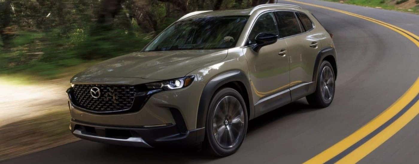 A green 2023 Mazda CX-50 is shown driving on a highway.