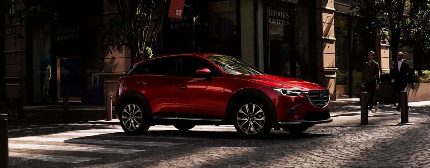 A red 2019 used Mazda CX-3 for sale near East Hartford in front of a shop.