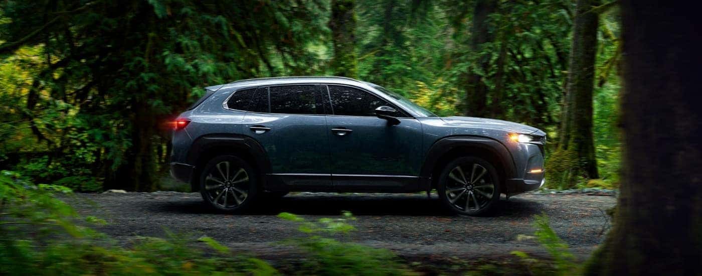 A blue 2023 Mazda CX-50 driving on a forest trail.