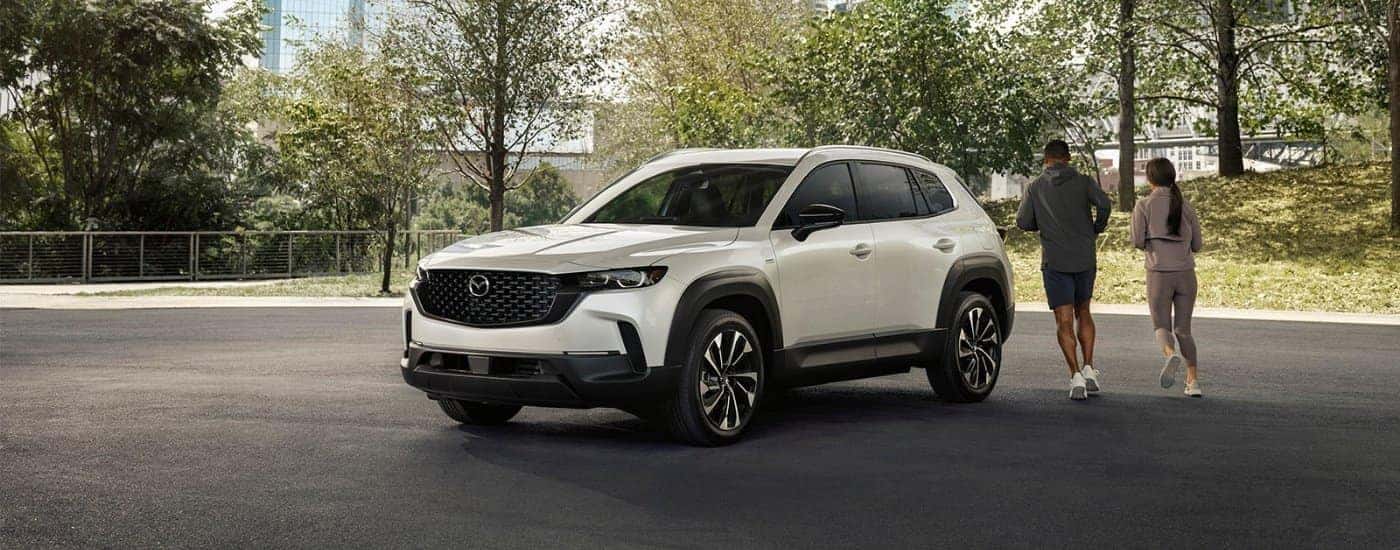 Joggers running past a white 2025 Mazda CX-50 for sale near Hartford.