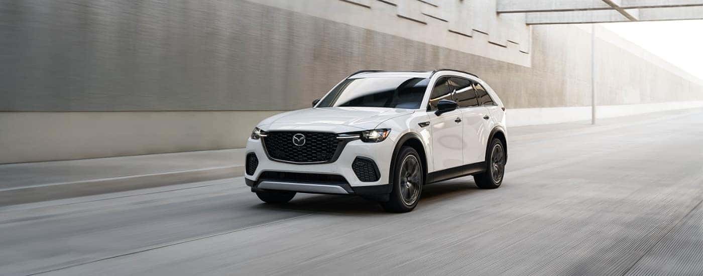 White 2025 Mazda CX-70 PHEV driving past a concrete wall