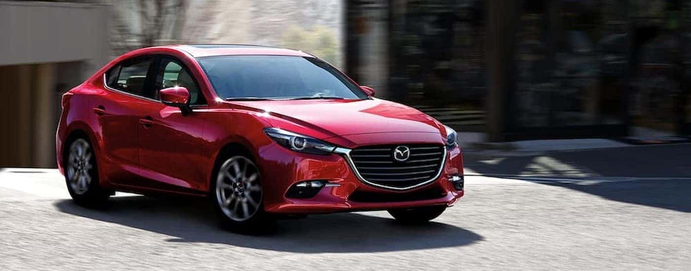 A red 2018 Mazda3 driving in a city.