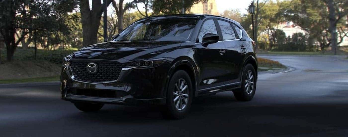 A black 2024 Mazda CX-5 is driving on a shady road.