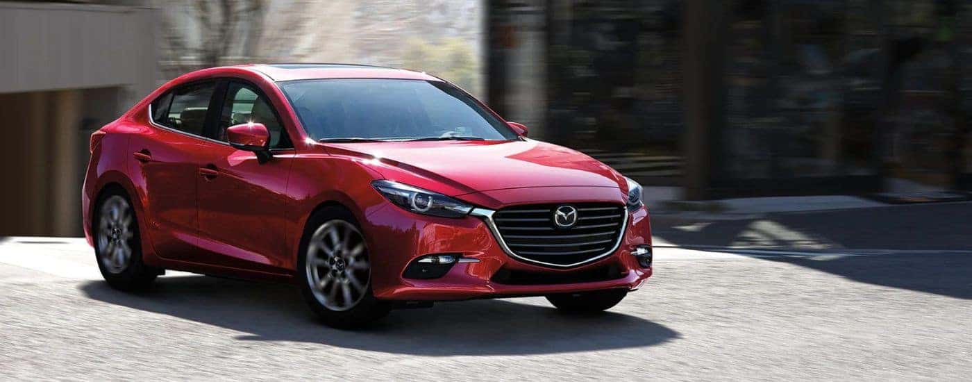 A red 2018 Mazda3 driving on a paved road.