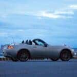 A light gray 2026 Mazda MX-5 Miata shown parked by water and a city.