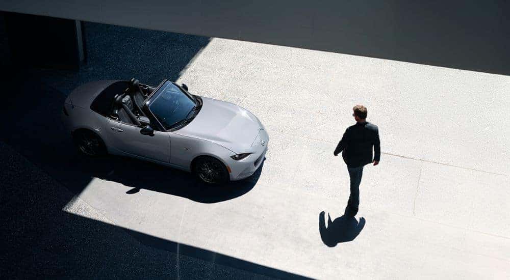 A person walking towards their silver 2026 Mazda MX-5 Miata with top down.