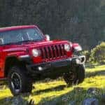 Red Jeep Wrangler Rubicon driving off-road in grassy mountains