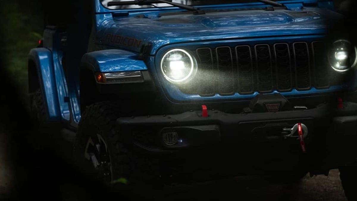 2026 Jeep Wrangler Rubicon front grille and headlights on a dark trail, RUBICON badge and winch visible