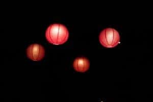 four paper lanterns illuminating a pitch black night sky