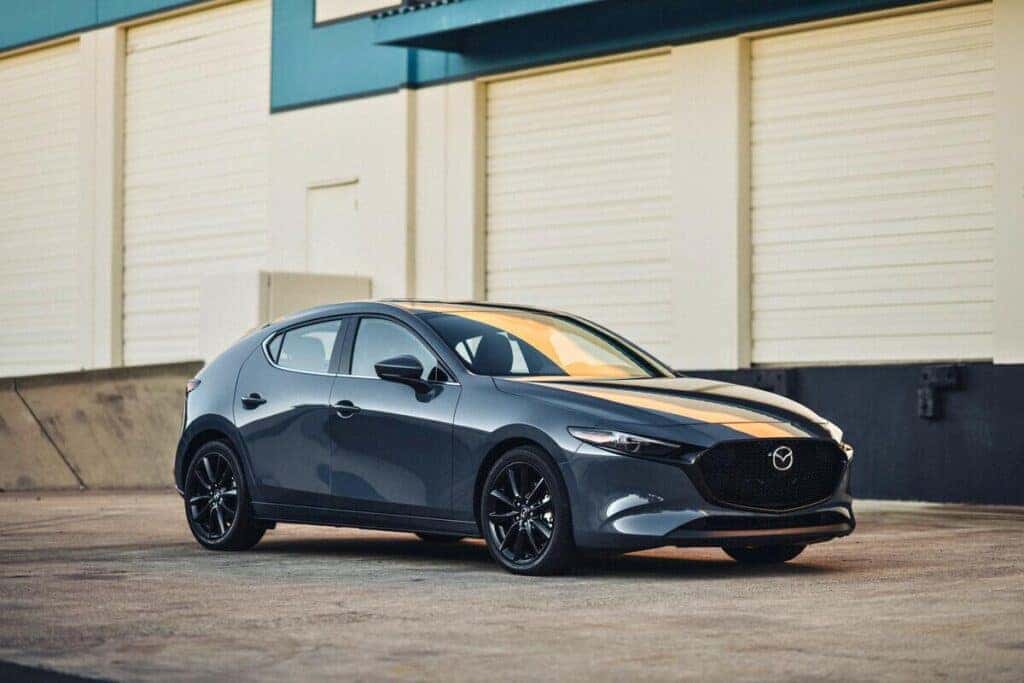 A Mazda 3 hatchback parked outside a warehouse, showcasing its stylish design and versatility.