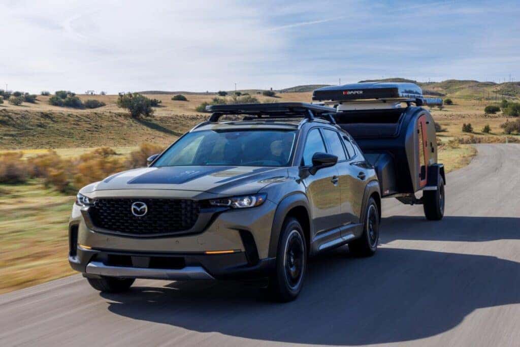 A 2025 Mazda CX-50 towing a trailer on a winding country road.