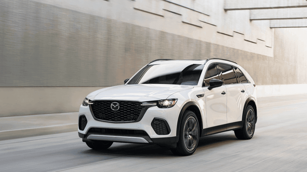 A 2025 Mazda CX-70 PHEV drives along a bustling city street, showcasing its sleek design and urban versatility.
