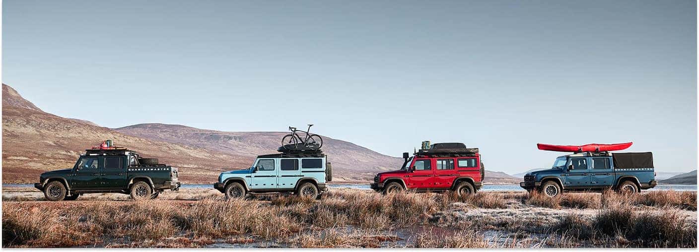 Side profile of a lineup of 2026 INEOS Grenadier Station Wagon models parked outdoors in a grassy field.