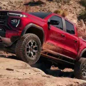 2026 GMC Canyon Volcanic Red Tintcoat driving on rocky terrain