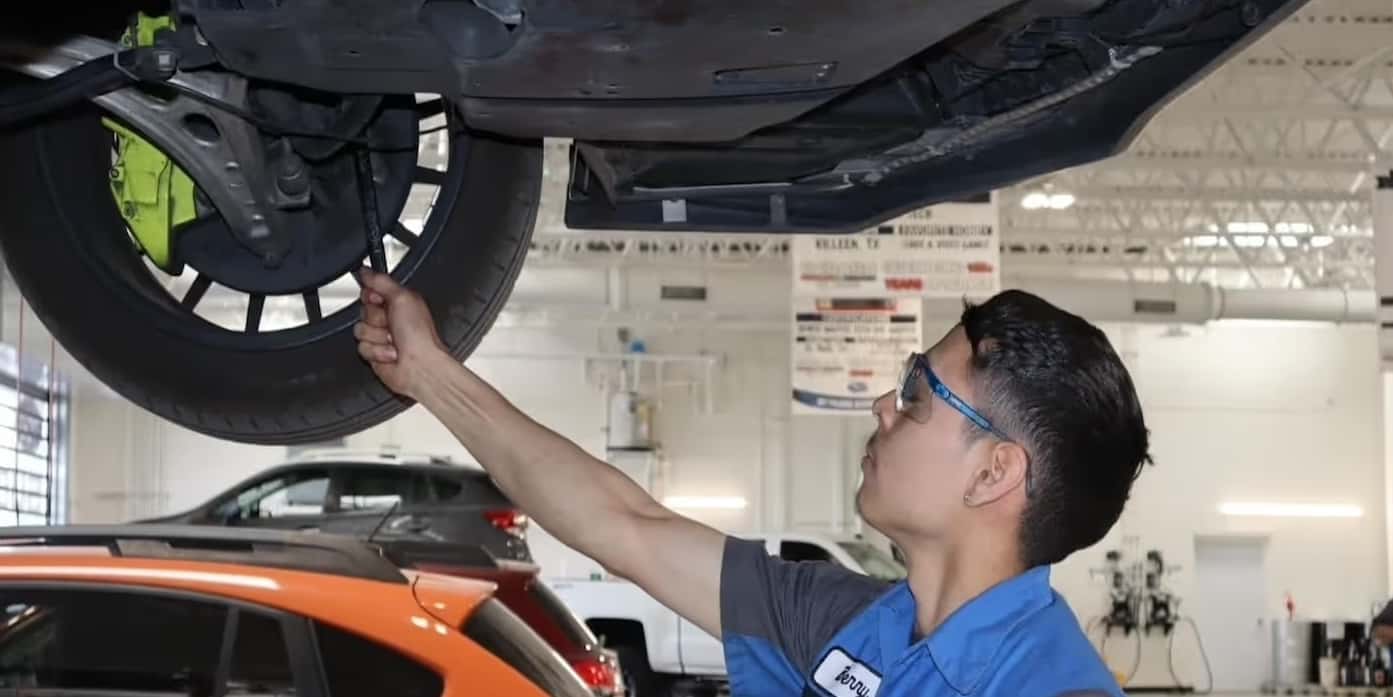 Service Tech looking under the hood of red vehicle in a service center.