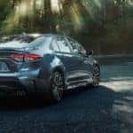 2020 Corolla from behind in forest with couple walking in background. 2020 Corolla MPG concept.