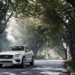 White Volvo XC60 driving down tree-lined street