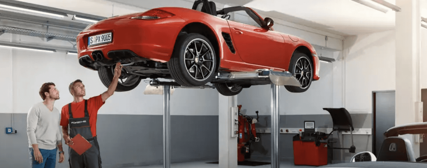 Porsche technician and customer look under a lifted up Porsche